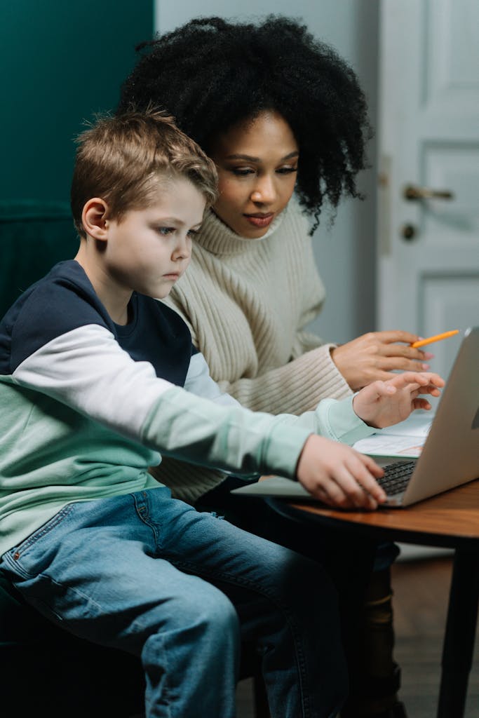 A teacher assists a child with homework using a laptop.  